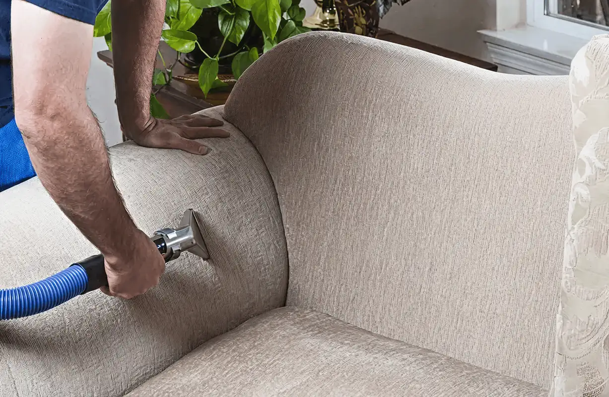 Professional upholstery cleaner deep-cleaning a fabric sofa with a handheld extraction tool and hose, Buffalo, NY.